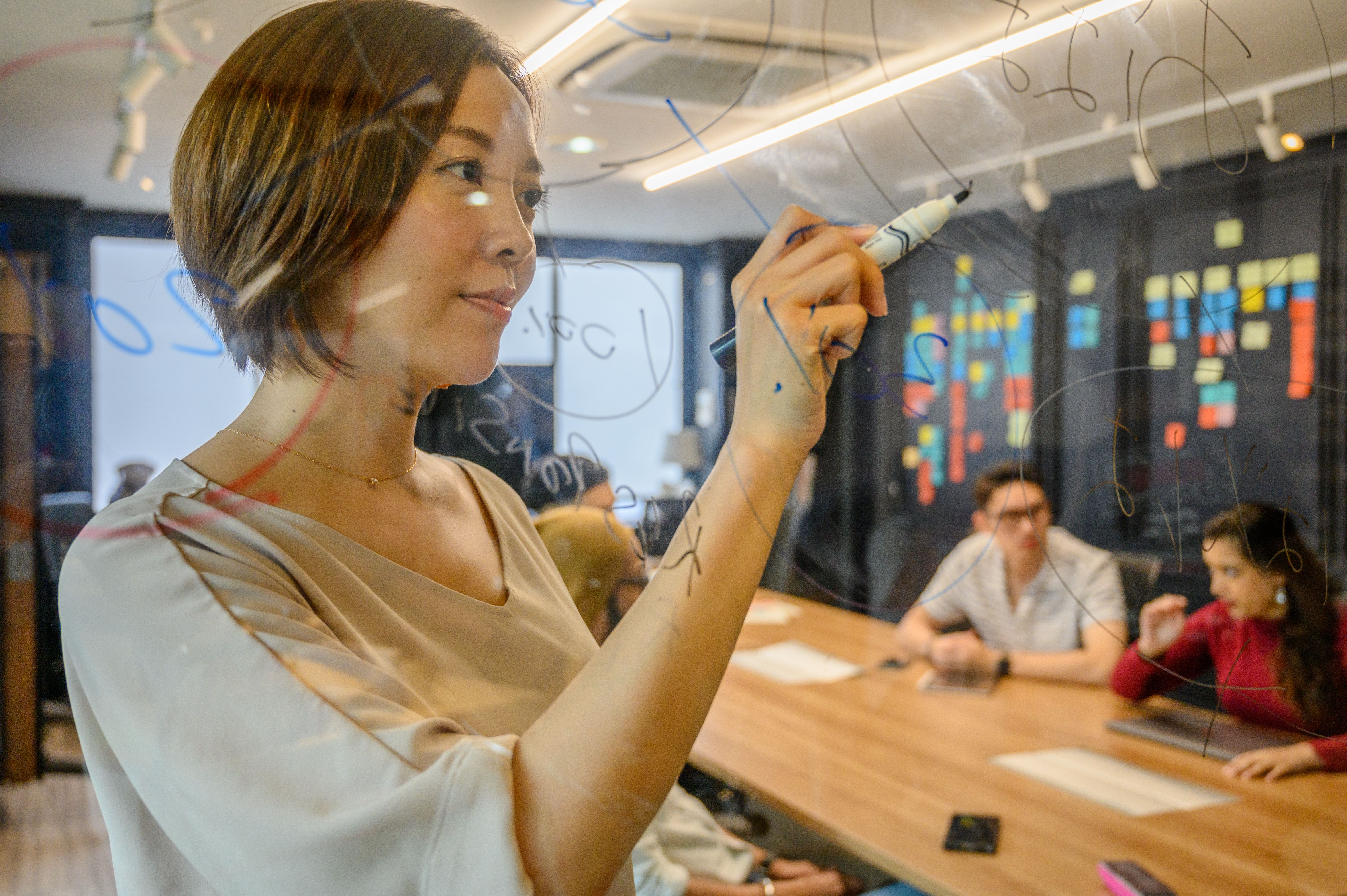 Professionals writing ideas on a glass board in a collaborative office, representing open communication at work.